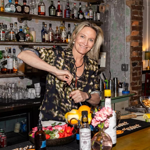 A smiling bartender in a leopard print shirt prepares a drink at a rustic bar.