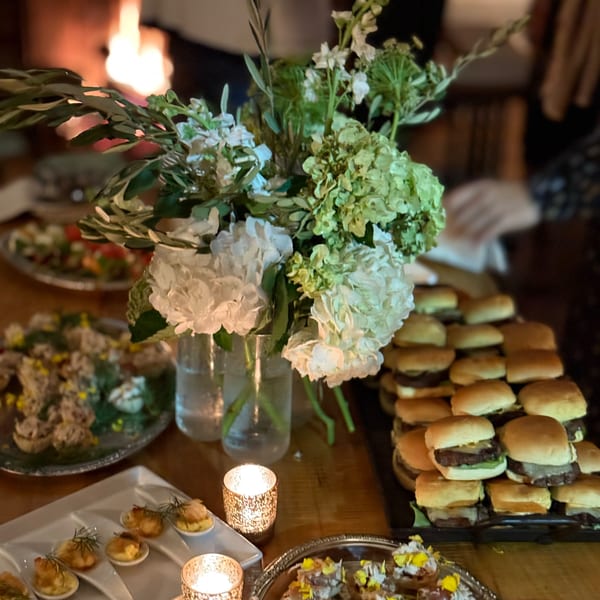 A table laden with appetizers, including sliders and small bites, with floral centerpieces and candles.