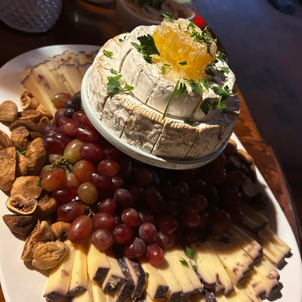 A cheese board with a wheel of brie topped with honeycomb, surrounded by grapes, figs, and sliced cheeses.