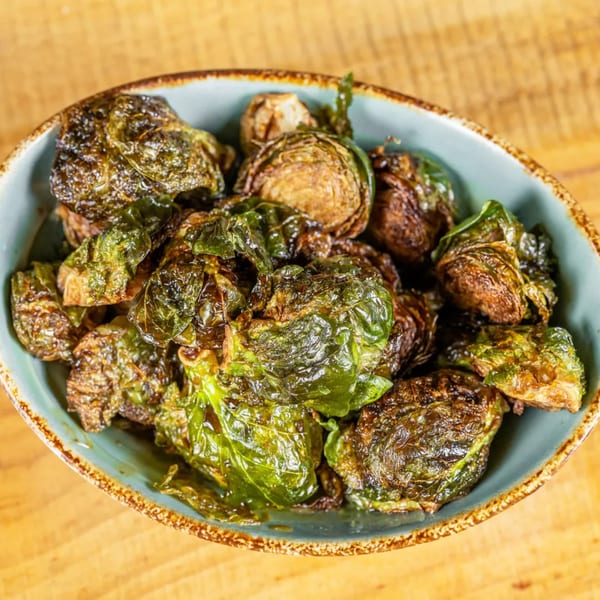 Close-up of crispy, roasted Brussels sprouts in a rustic blue bowl on a wooden surface.