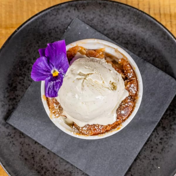 Warm apple crumble with a scoop of vanilla bean ice cream and a purple edible flower.