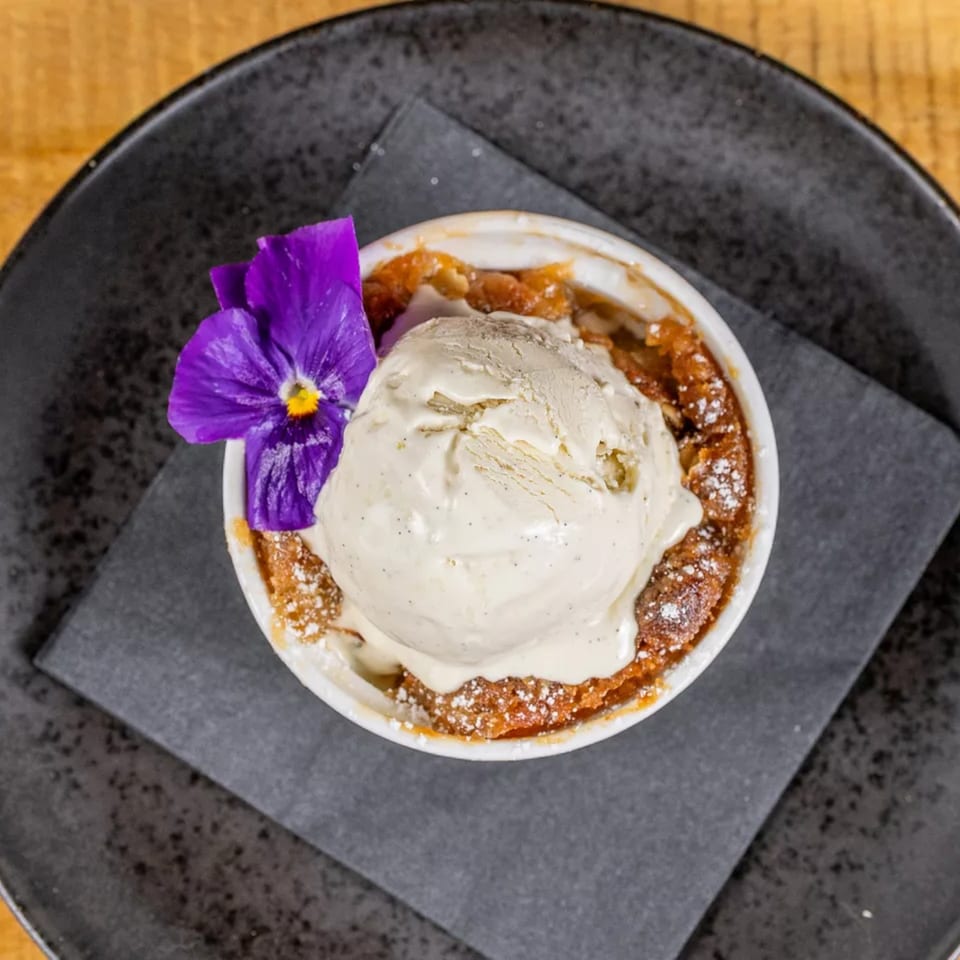Warm apple crumble with a scoop of vanilla bean ice cream and a purple edible flower.