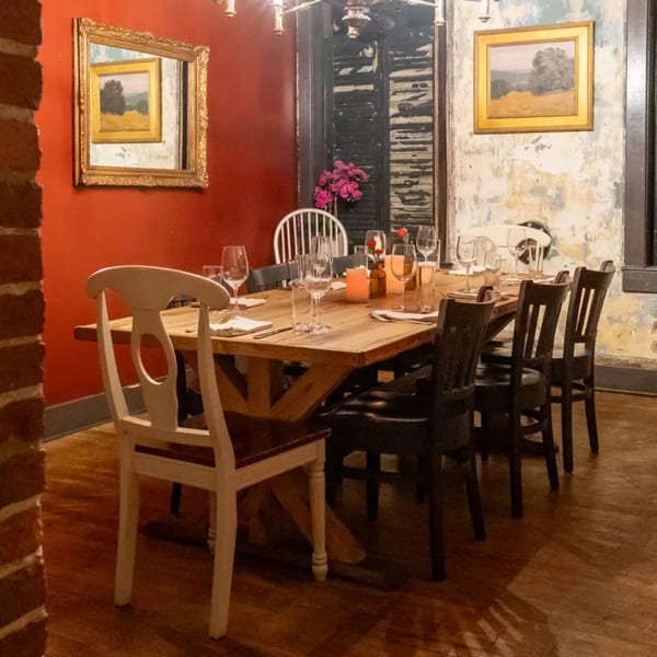 A rustic dining room with a long wooden table set for dinner, surrounded by chairs.