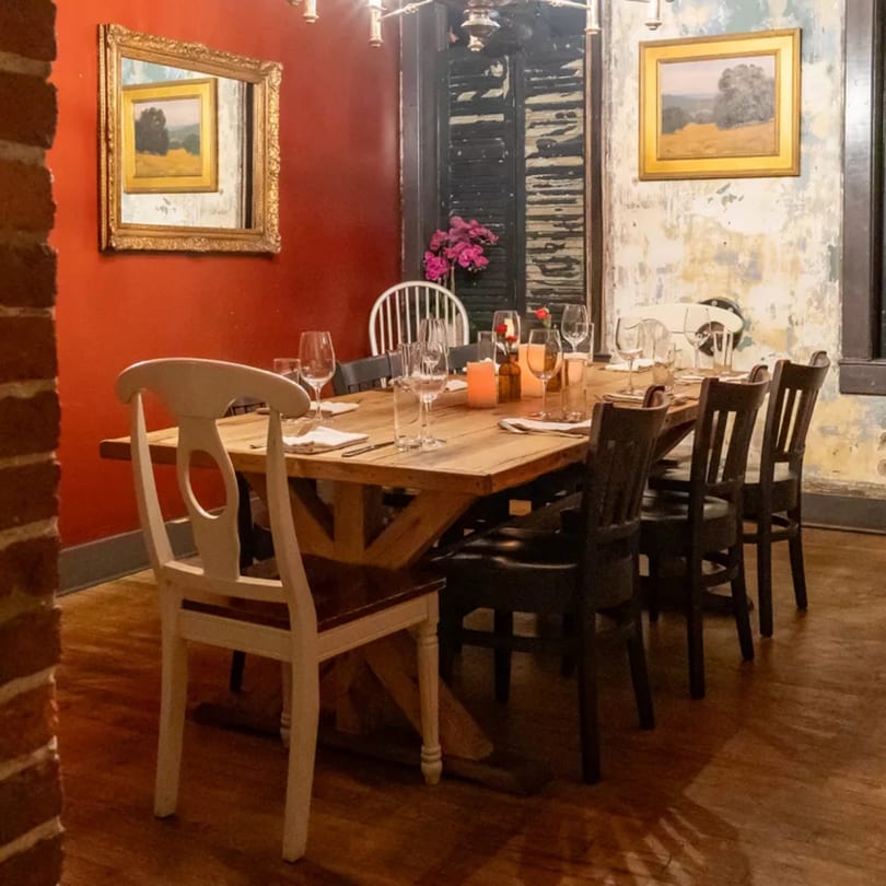 A rustic dining room with a long wooden table set for dinner, surrounded by chairs.