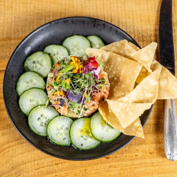 Salmon tartare with microgreens and edible flowers, surrounded by cucumber slices and tortilla chips.