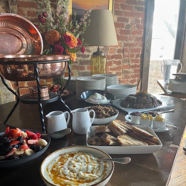 A buffet table laden with breakfast foods, including fruit, yogurt, granola, pastries, and toast.